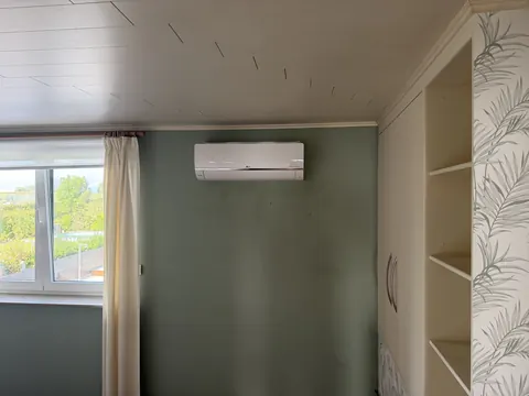 Binnenunit aan een groene muur naast het raam