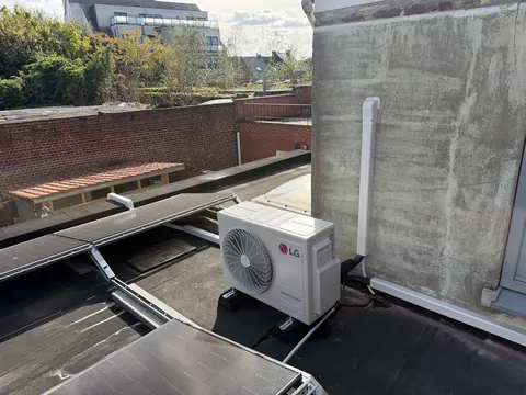 Buitenunit op een plat dak, de leiding in een goot langs de muur