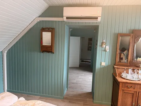 Binnenunit op een zolderkamer met groene lambrisering, de leiding netjes in een goot