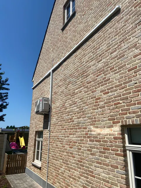 Buitenunit hoog aan een bakstenen zijgevel