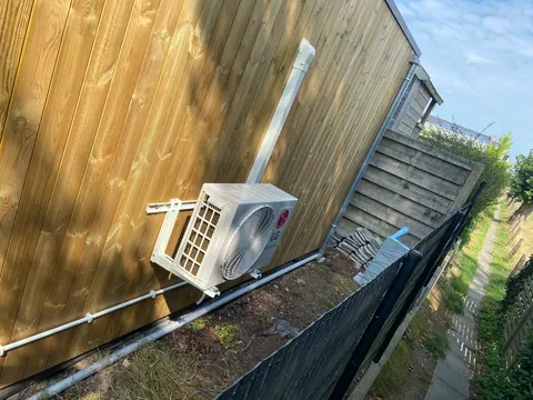 Buitenunit op een plat dak naast een houten gevel