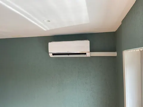 Binnenunit aan een groene muur, de leiding netjes in een goot