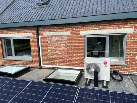 Buitenunit op een plat dak naast lichtkoepels en zonnepanelen