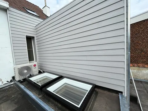 Buitenunit op een plat dak naast lichtkoepels