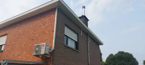 Buitenunit aan een bakstenen gevel onder het dak