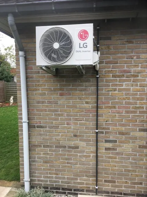 Buitenunit aan een gele bakstenen gevel, de afvoer langs de regenpijp